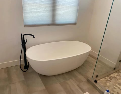 Modern white oval freestanding bathtub in a minimalist bathroom with wood flooring and glass shower enclosure