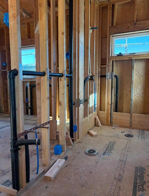 Interior of a house under construction showing wooden framing, studs, windows, and PVC plumbing pipes during renovation