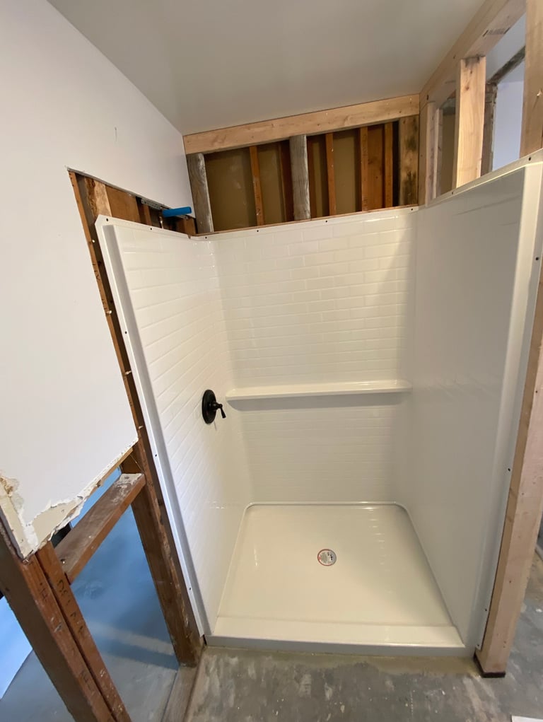 White prefab shower stall being installed in bathroom under construction with exposed framing visible above