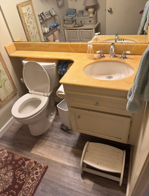 Small bathroom interior with light wood vanity sink, toilet, and storage shelves in background