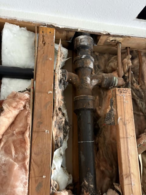 Corroded metal pipe fixture inside wooden cavity with insulation material and deteriorated components