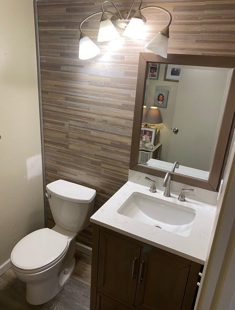 Modern bathroom with white toilet, dark vanity with sink, framed mirror, and wall-mounted light fixture on striped tile backdrop
