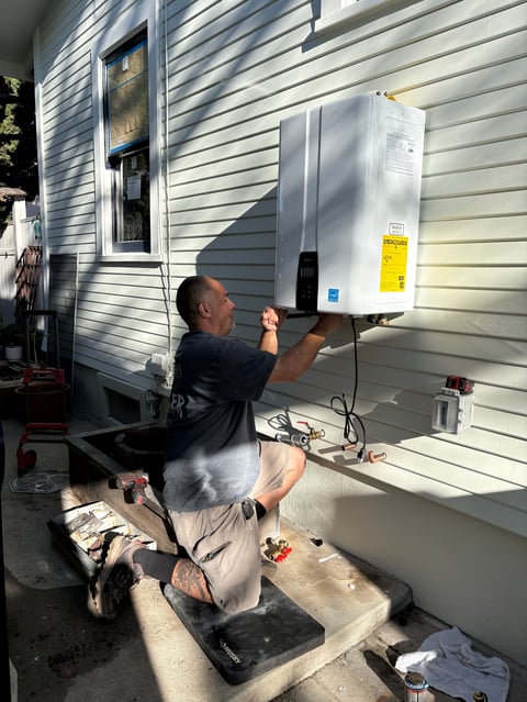 Technician installing a white heat pump unit on the side of a house with vinyl siding