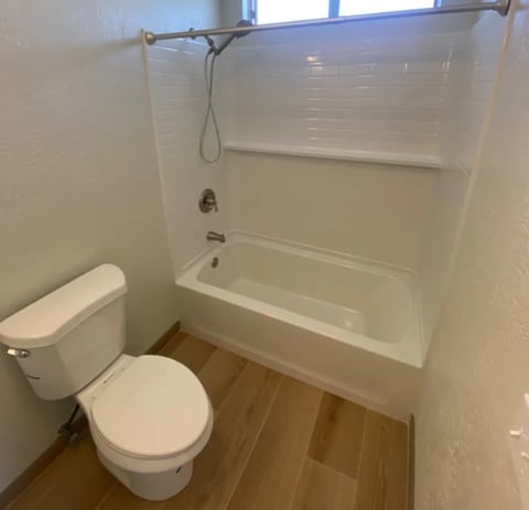 Small bathroom with white toilet, bathtub with shower enclosure, and wood-look flooring